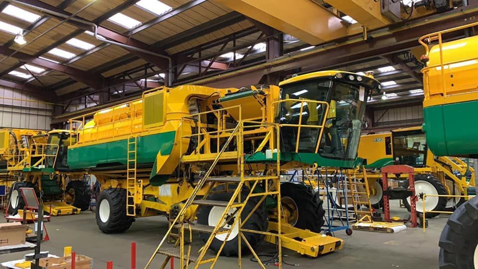 Una grande mietitrebbia gialla e verde è in riparazione in una fabbrica.
