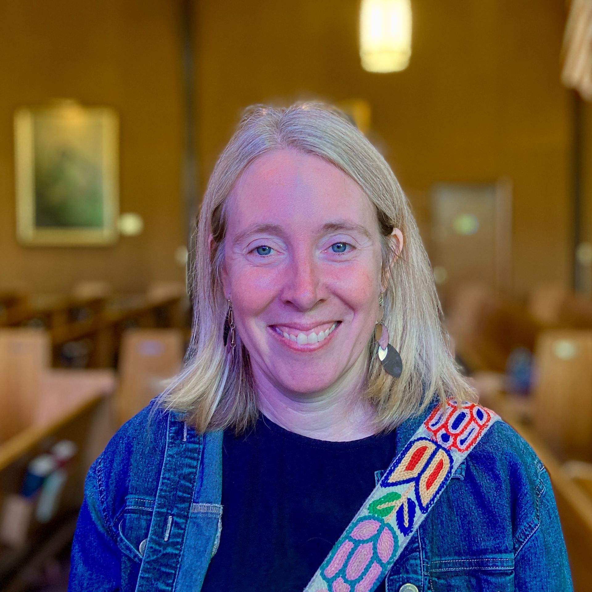 A woman wearing a denim jacket and a black shirt smiles for the camera
