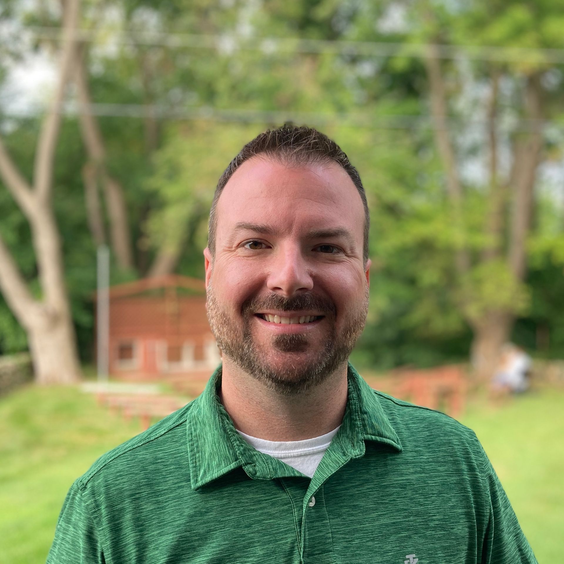 A man with a beard is wearing a green shirt and smiling.
