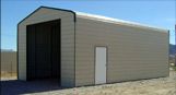 A large metal building with a large door is sitting on top of a dirt field.