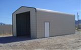 A small building with a large door is sitting in the middle of a dirt field.