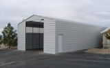 A white garage with a black door is sitting next to a house.