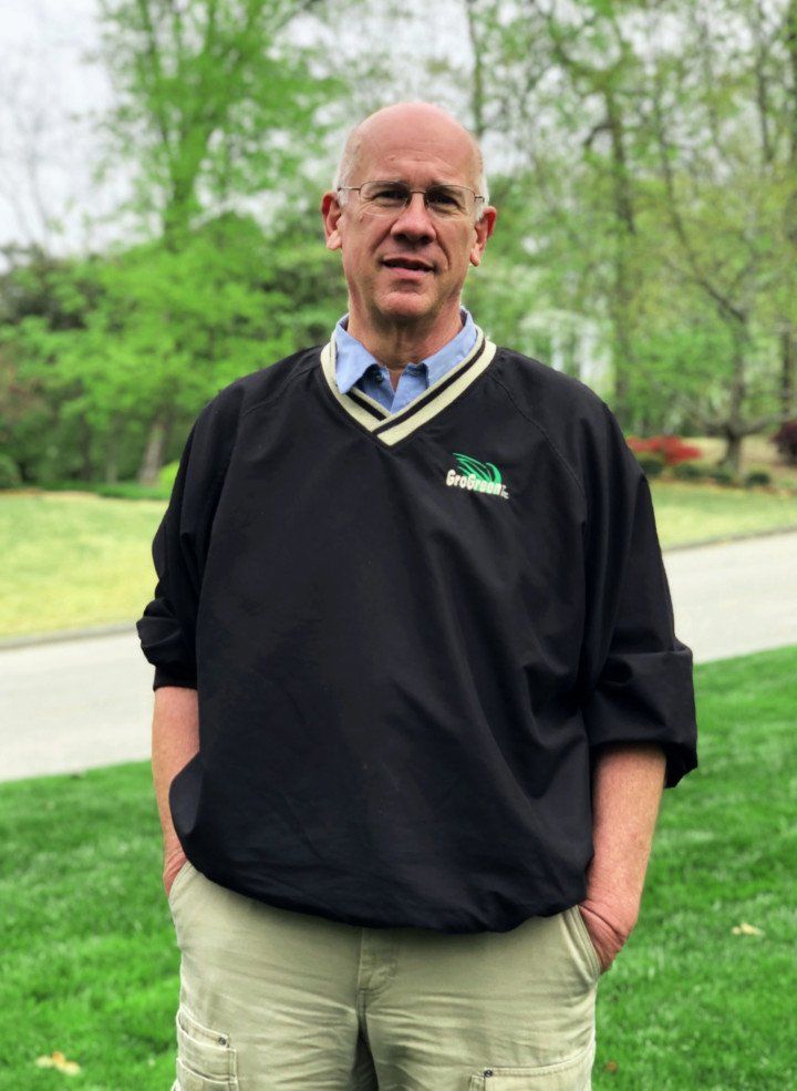 A man wearing a black sweater and khaki pants is standing in a grassy field.