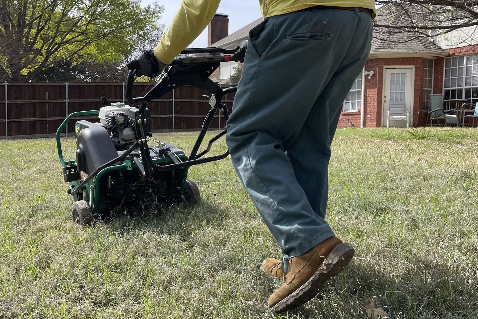 Person using a green lawn aerator on a patchy lawn in front of a house.