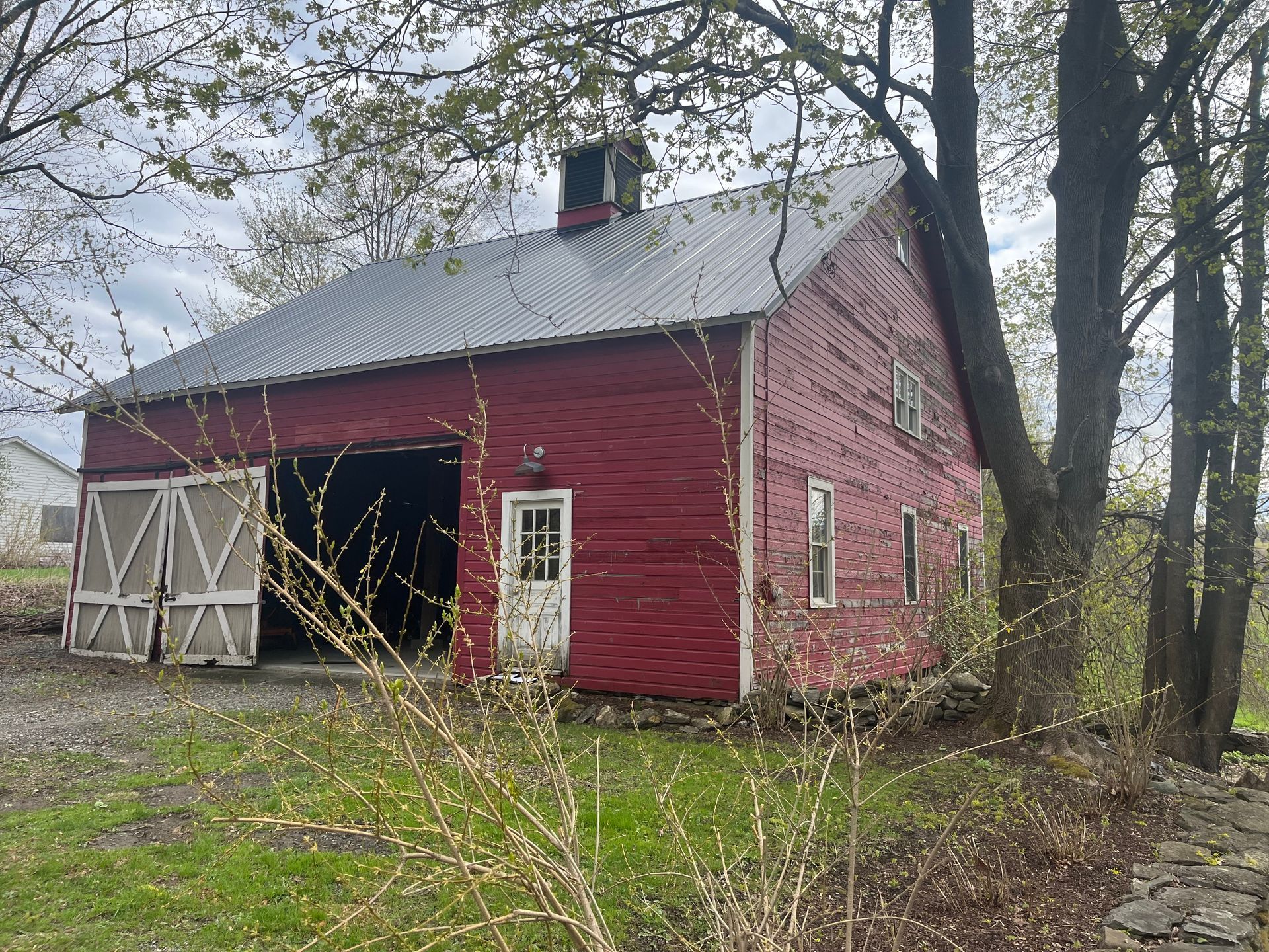 A red barn with a metal roof is surrounded by trees.