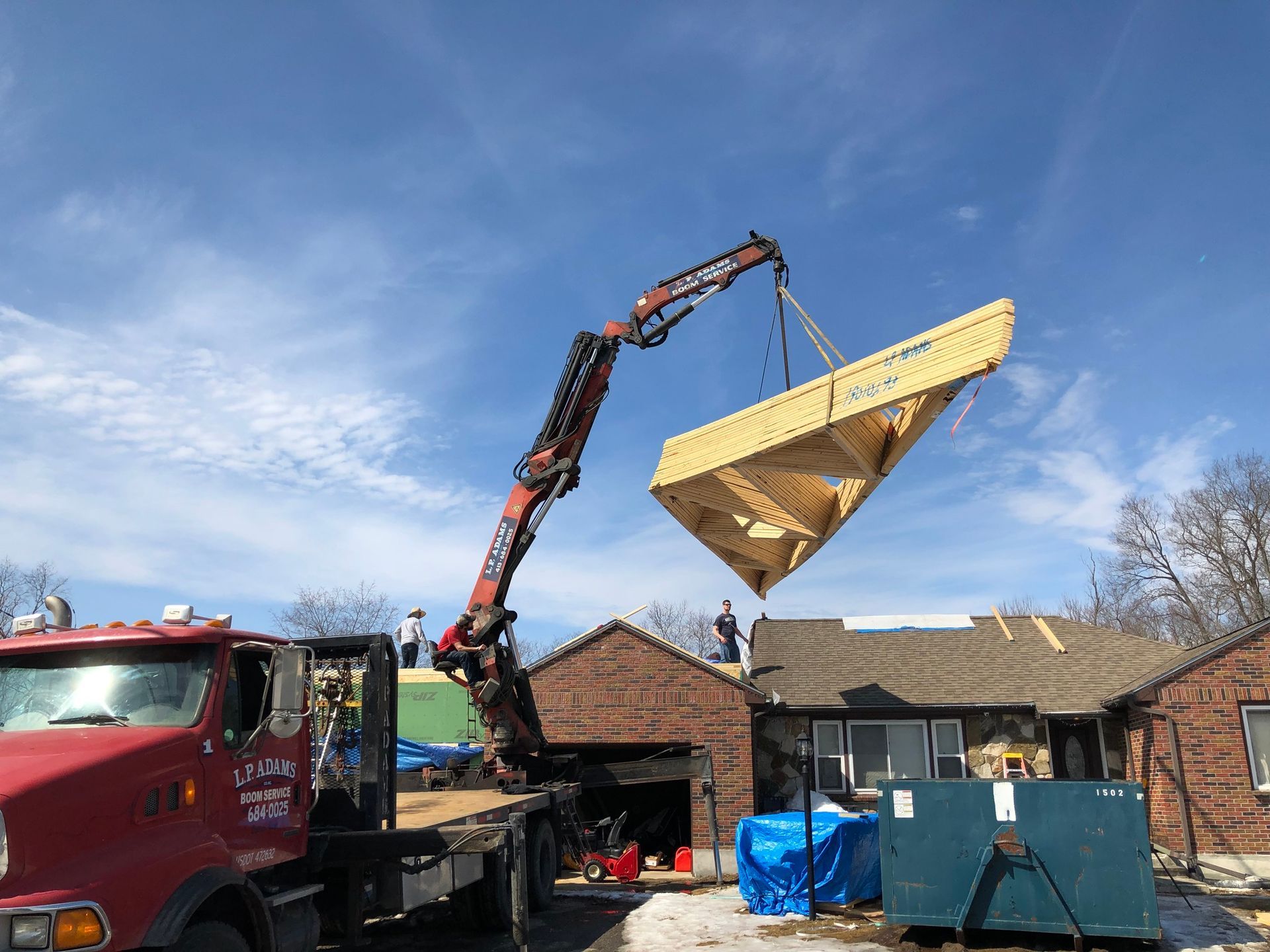 A crane is lifting a large piece of wood over a house.