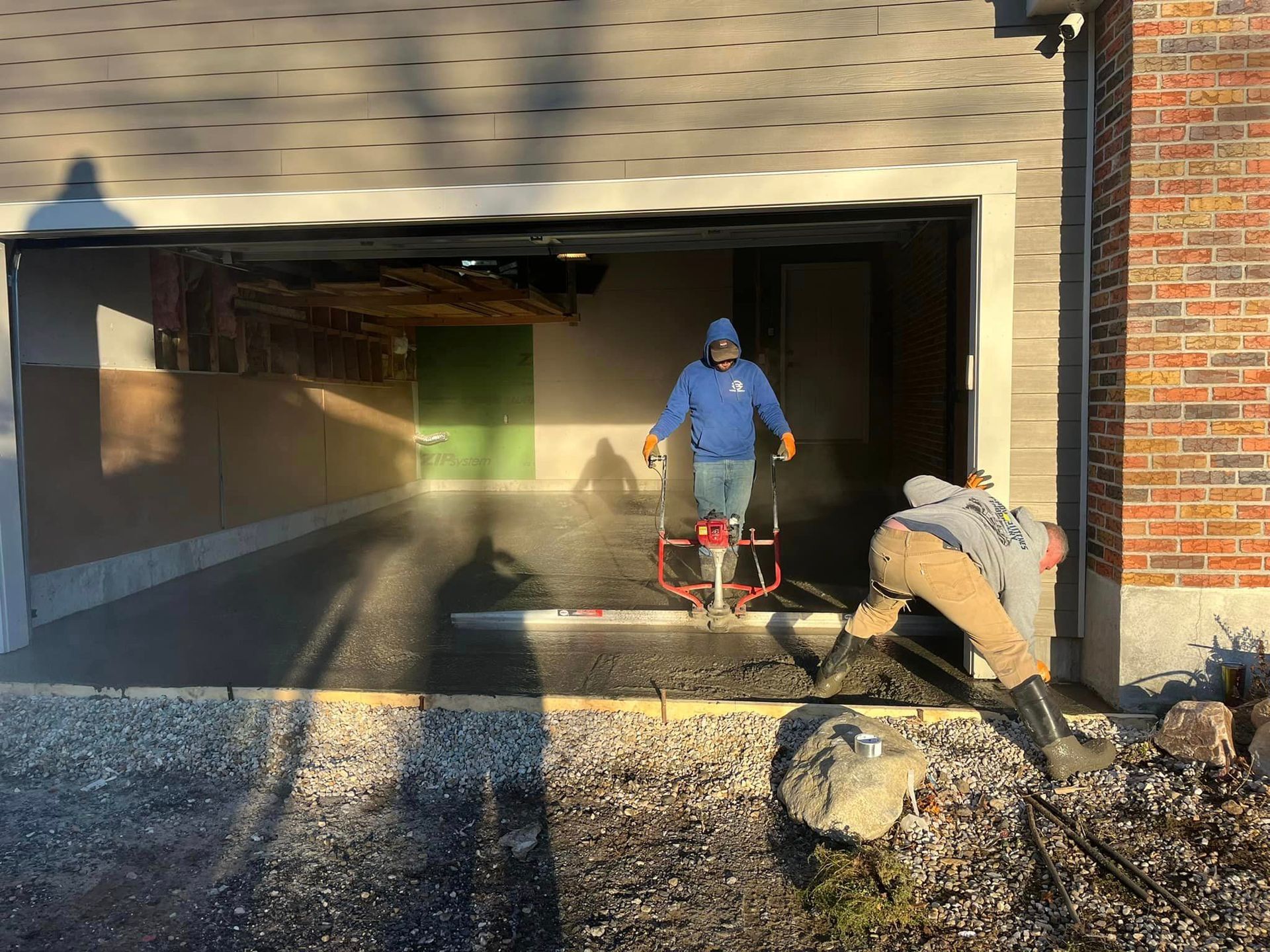 Two men are working on a driveway in front of a garage.