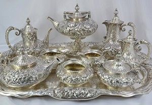 Silver tea set on a tray, with ornate floral details, including teapot, sugar bowl, and creamer.