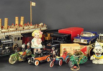 Collection of antique toy cars, motorcycles, a doll, and a boat on a dark surface.