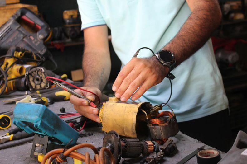 Persona utilizando un multímetro para probar un motor eléctrico en un banco de trabajo con herramientas.