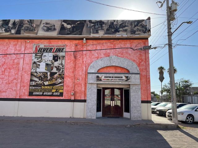 Edificio comercial rosa con un letrero de la Línea Plateada, entrada arqueada y coches aparcados.