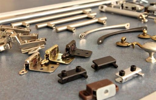 Diversos herrajes y componentes metálicos para gabinetes sobre una superficie gris.