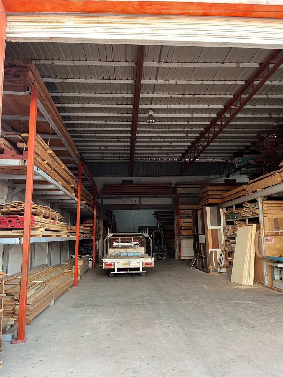 Vista interior de un aserradero con estanterías llenas de madera, un camión y un techo de metal.