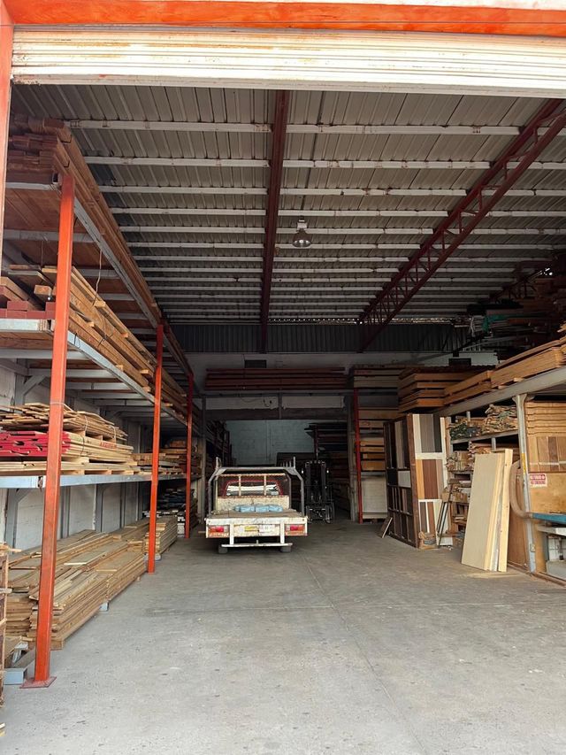 Vista interior de un aserradero con estanterías llenas de madera, un camión y un techo de metal.
