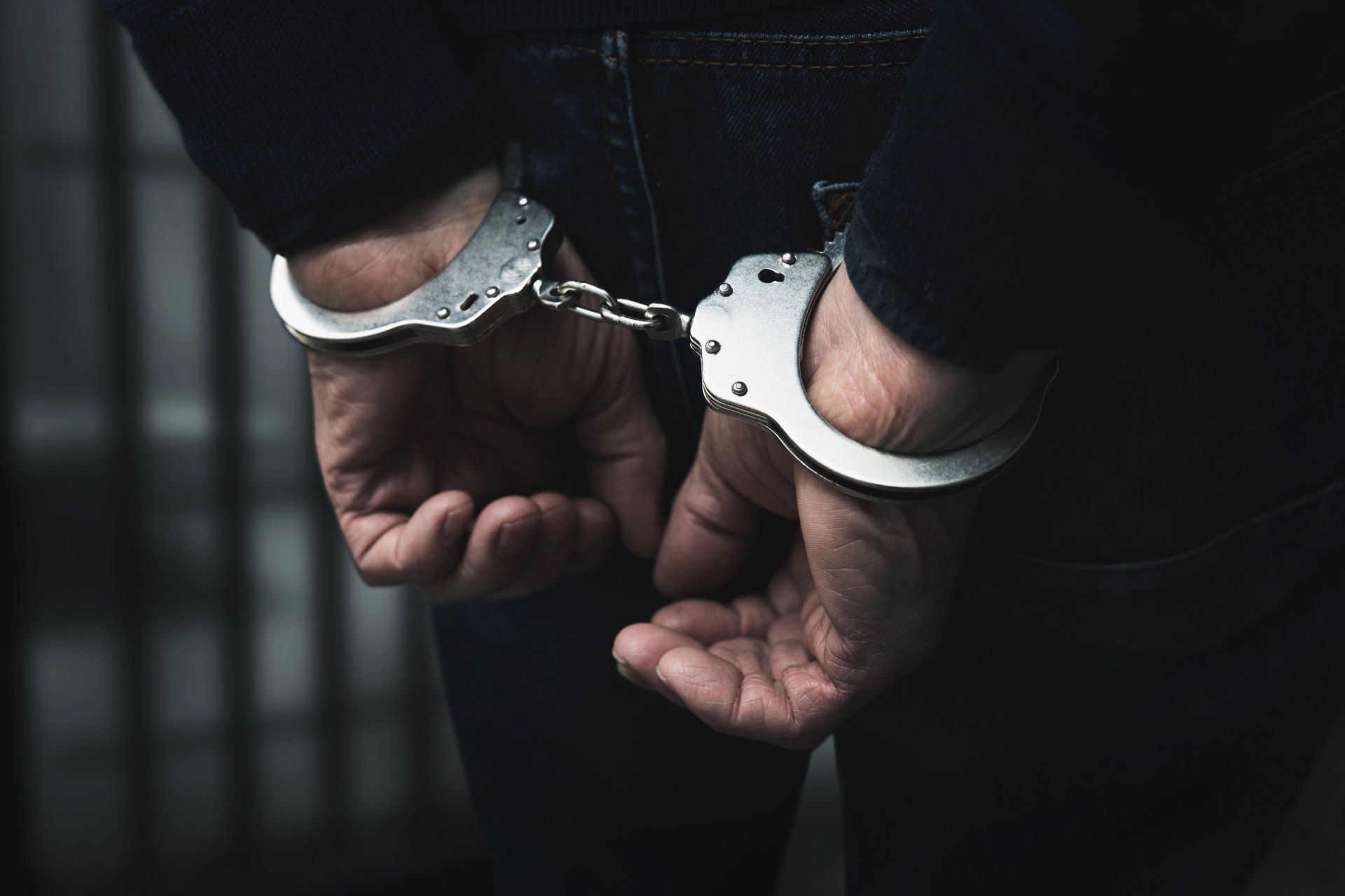 A man in handcuffs is standing in a dark room.