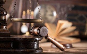 A wooden gavel is sitting on a wooden table next to a scale of justice.