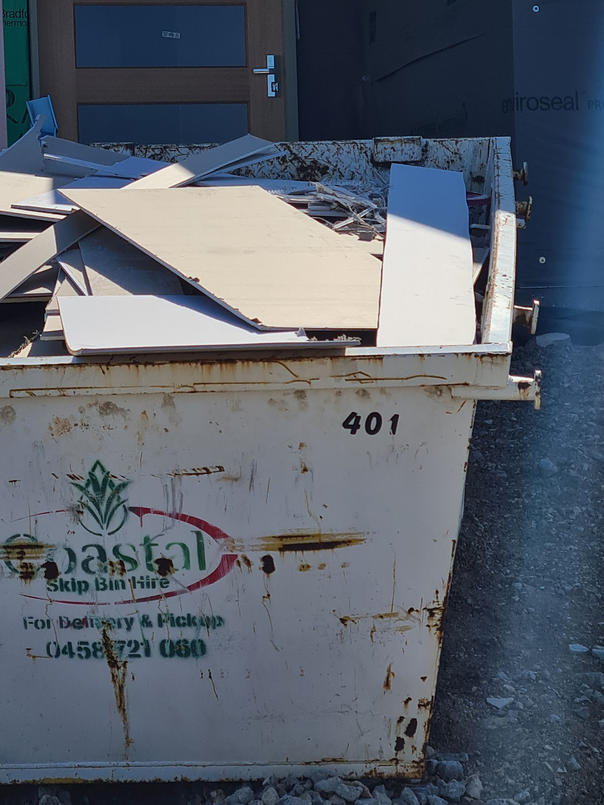 A white garbage truck beside a construction site, with a large dumpster on a sunny day. — Coastal Skip Bin Hire In Point Vernon, QLD