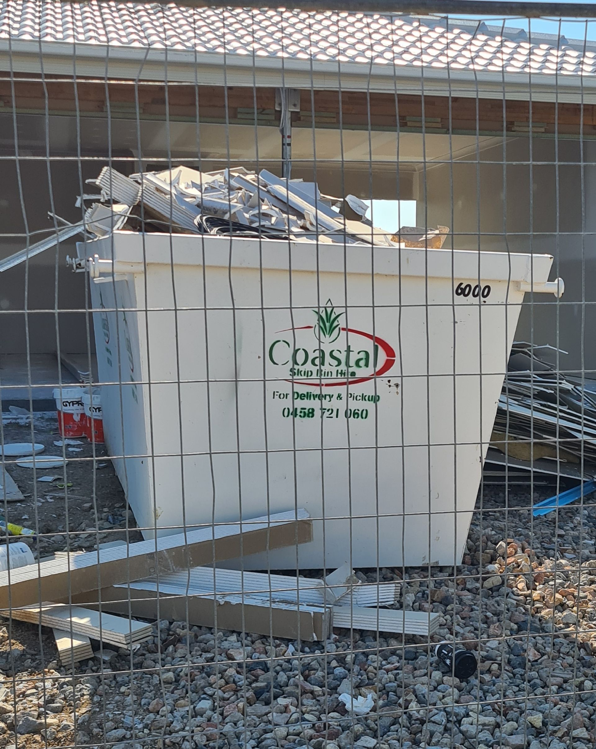 White Coastal Skip Bins dumpster. Green logo, red text. Outdoors, construction site. — Coastal Skip Bin Hire In Point Vernon, QLD