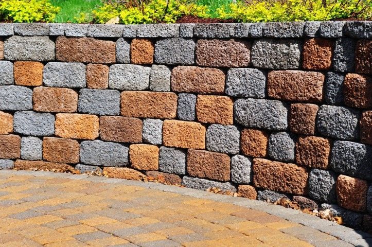 Curved stone retaining wall made of gray, tan, and brown blocks beside a paved walkway