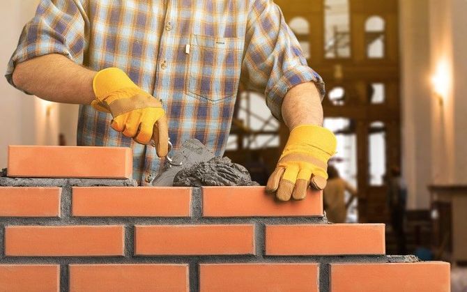 Gloved hands laying bricks on a brick wall with mortar in a construction site