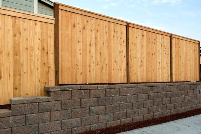 Wooden privacy fence above a gray block retaining wall beside a paved walkway.
