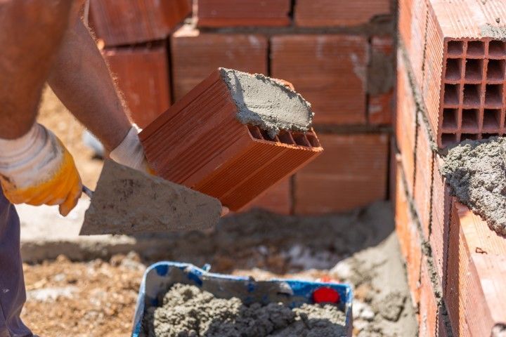 Worker laying red bricks with gray mortar at a construction site