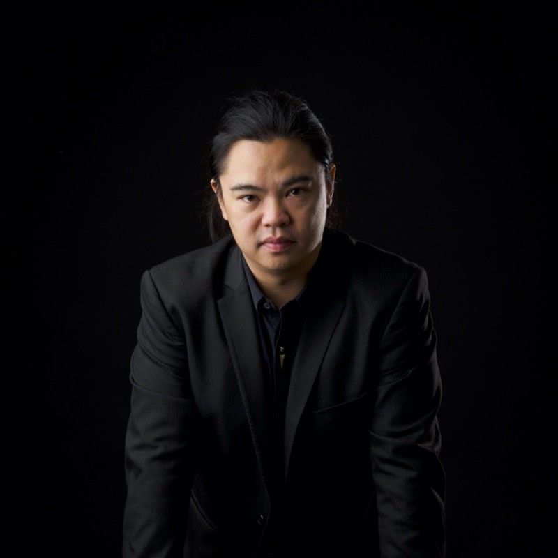 A trainer in a black suit is kneeling down in front of a black background.
