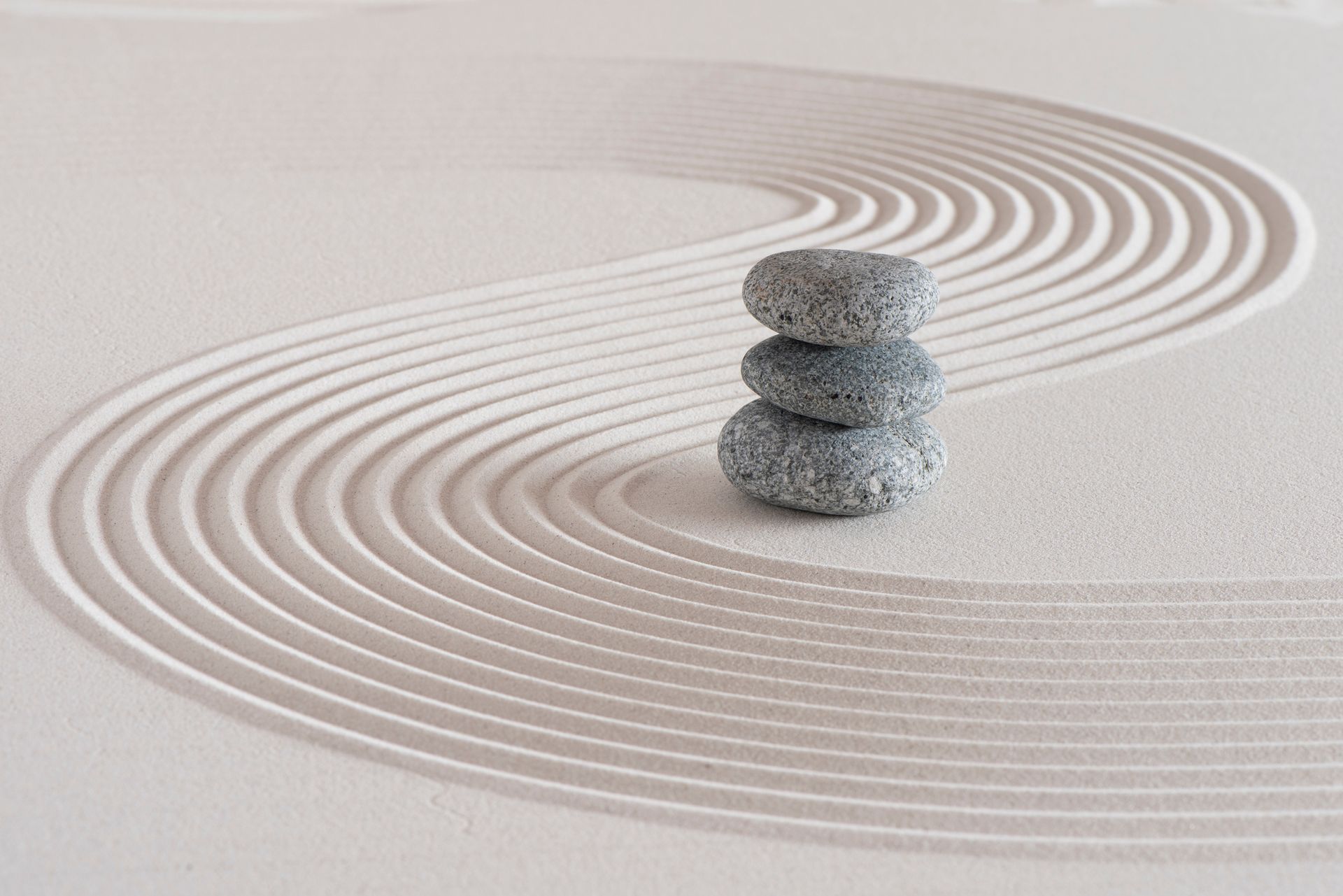Three rocks are stacked on top of each other in a sandy garden.