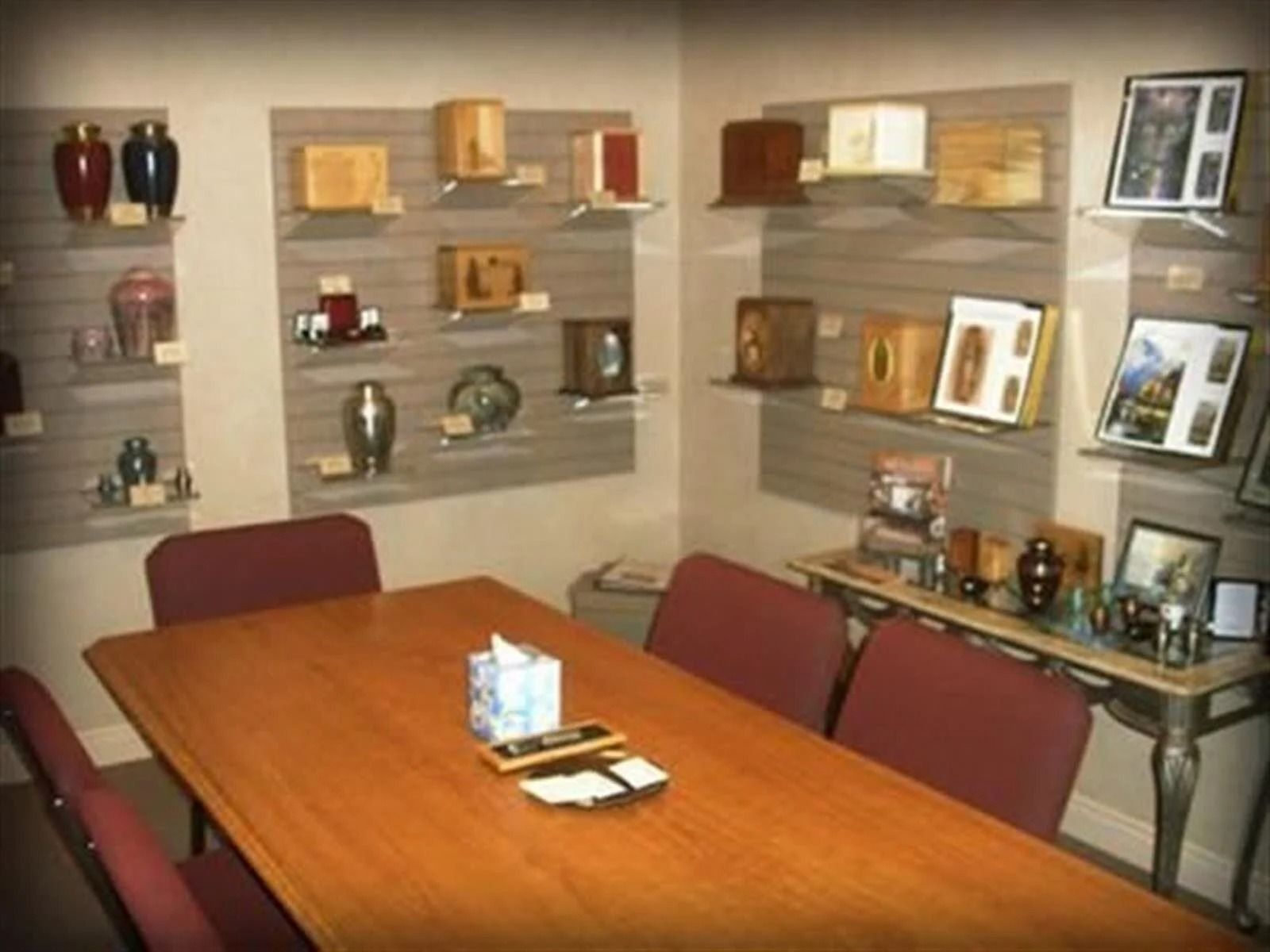 A room with a table, chairs, and shelves displaying urns.