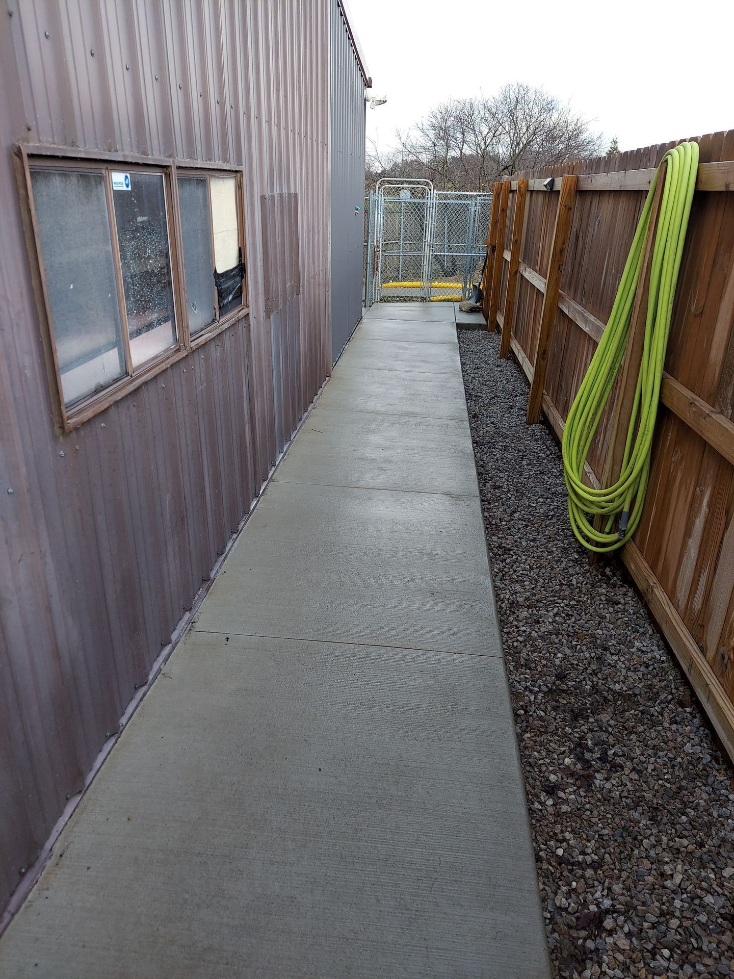 A concrete walkway leading to a wooden fence next to a building.