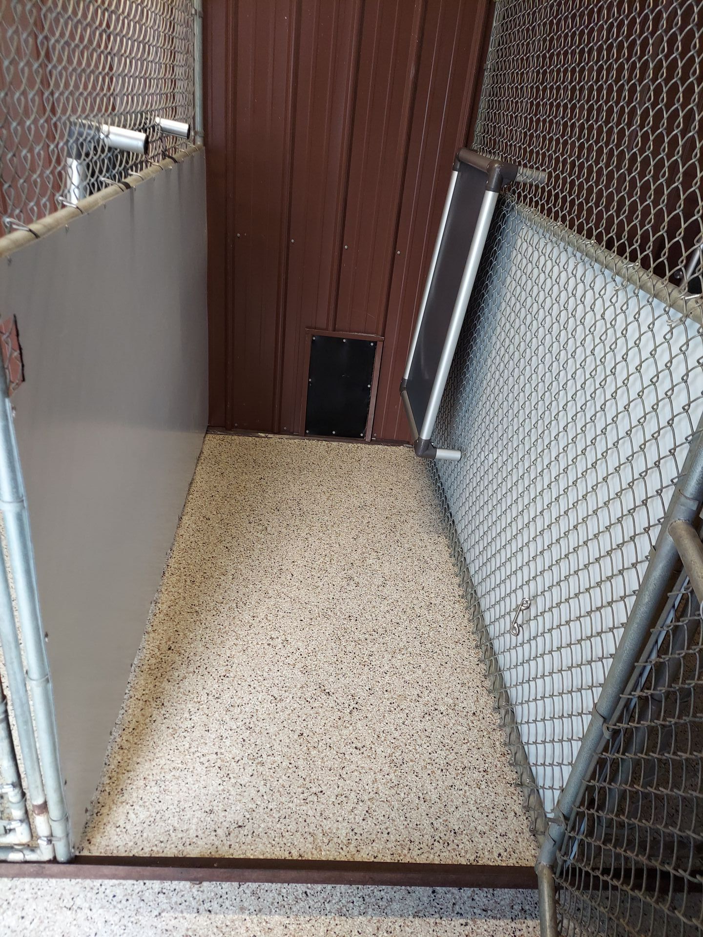 A dog kennel with a chain link fence and a dog door.