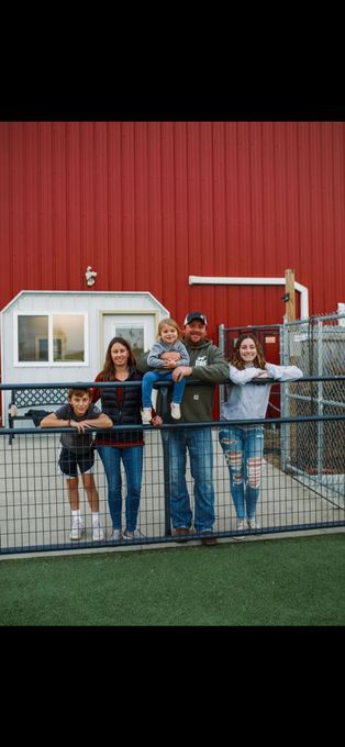 A family is standing on a fence in front of a red building.