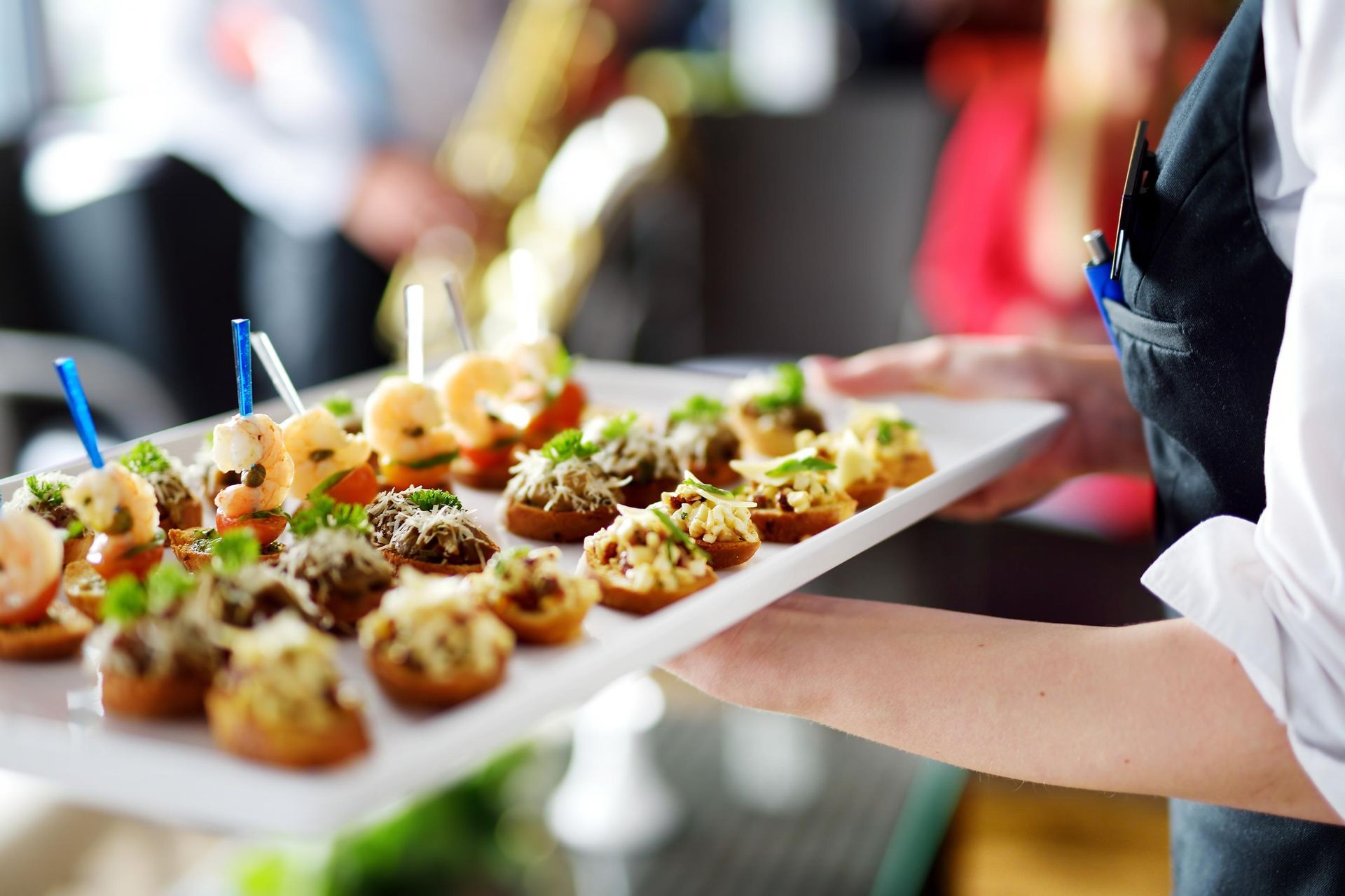 Tray of bite-sized appetizers garnished with herbs, held by a server at a catered event