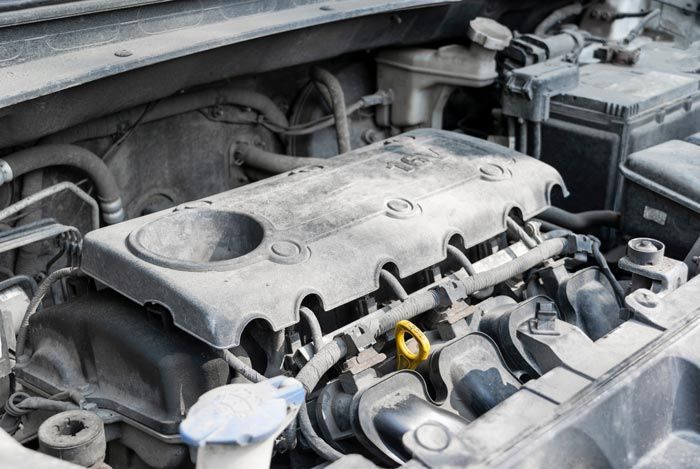 A close up of a dirty car engine with the hood open.