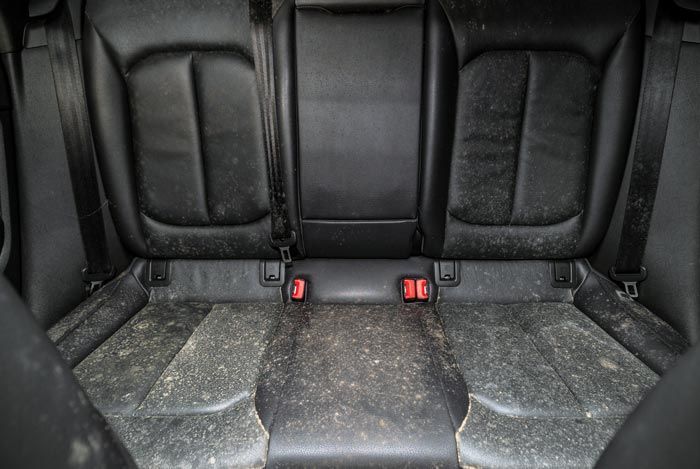 The back seat of a car is dirty and covered in dust.