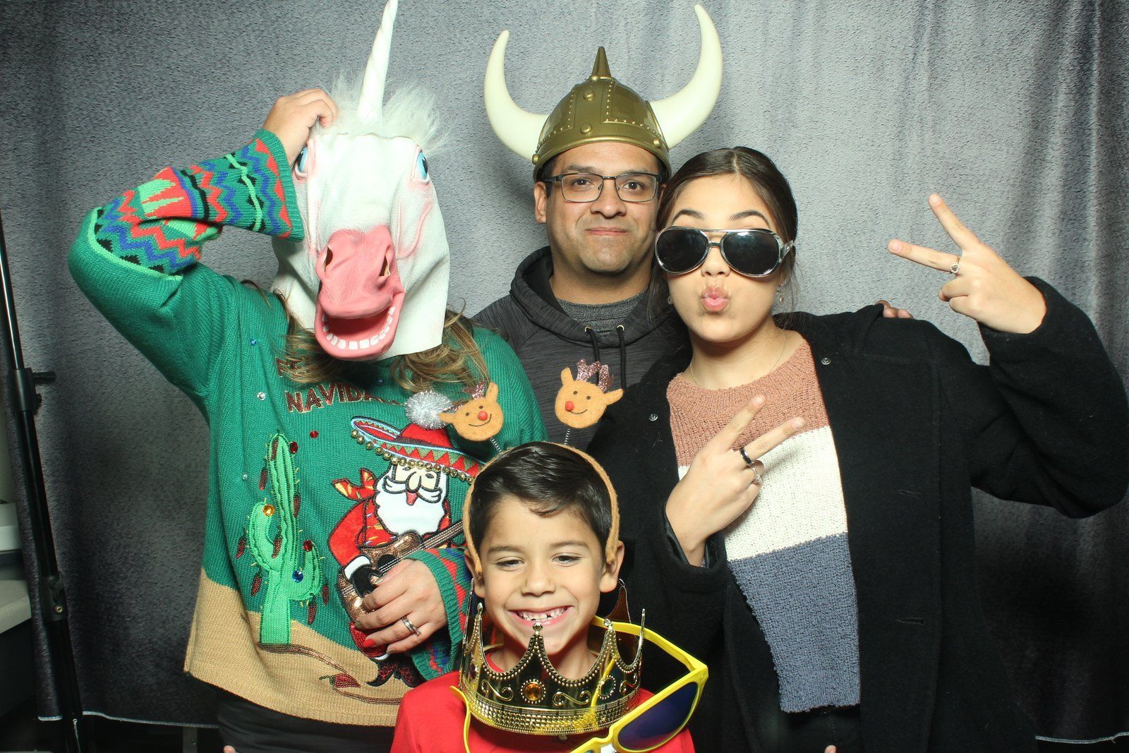 Four people in front of a shiny backdrop, wearing oversized novelty glasses and a gold hat, around a microphone.