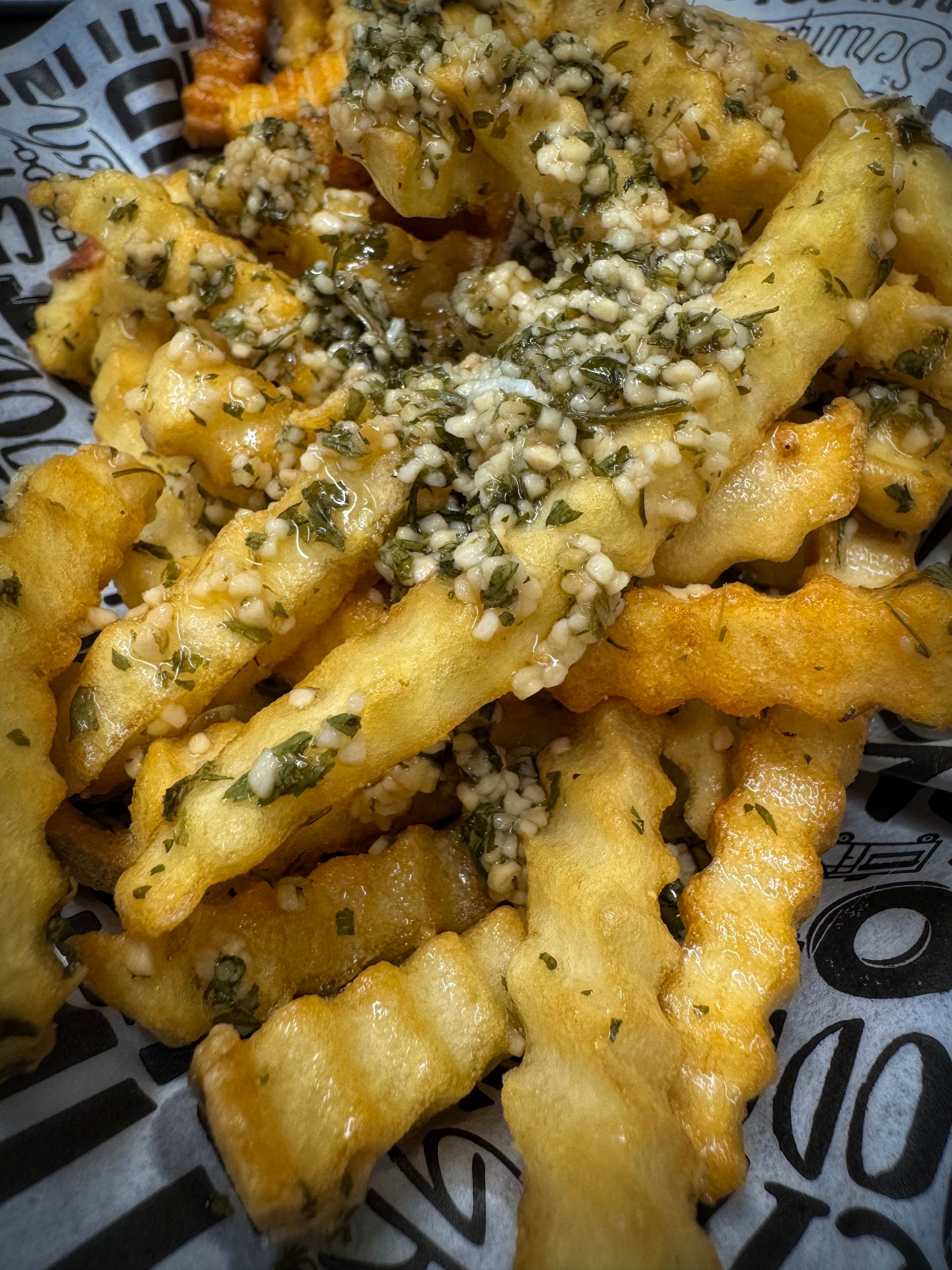 Crinkle-cut fries topped with garlic, herbs, and sauce served in a basket on patterned paper.