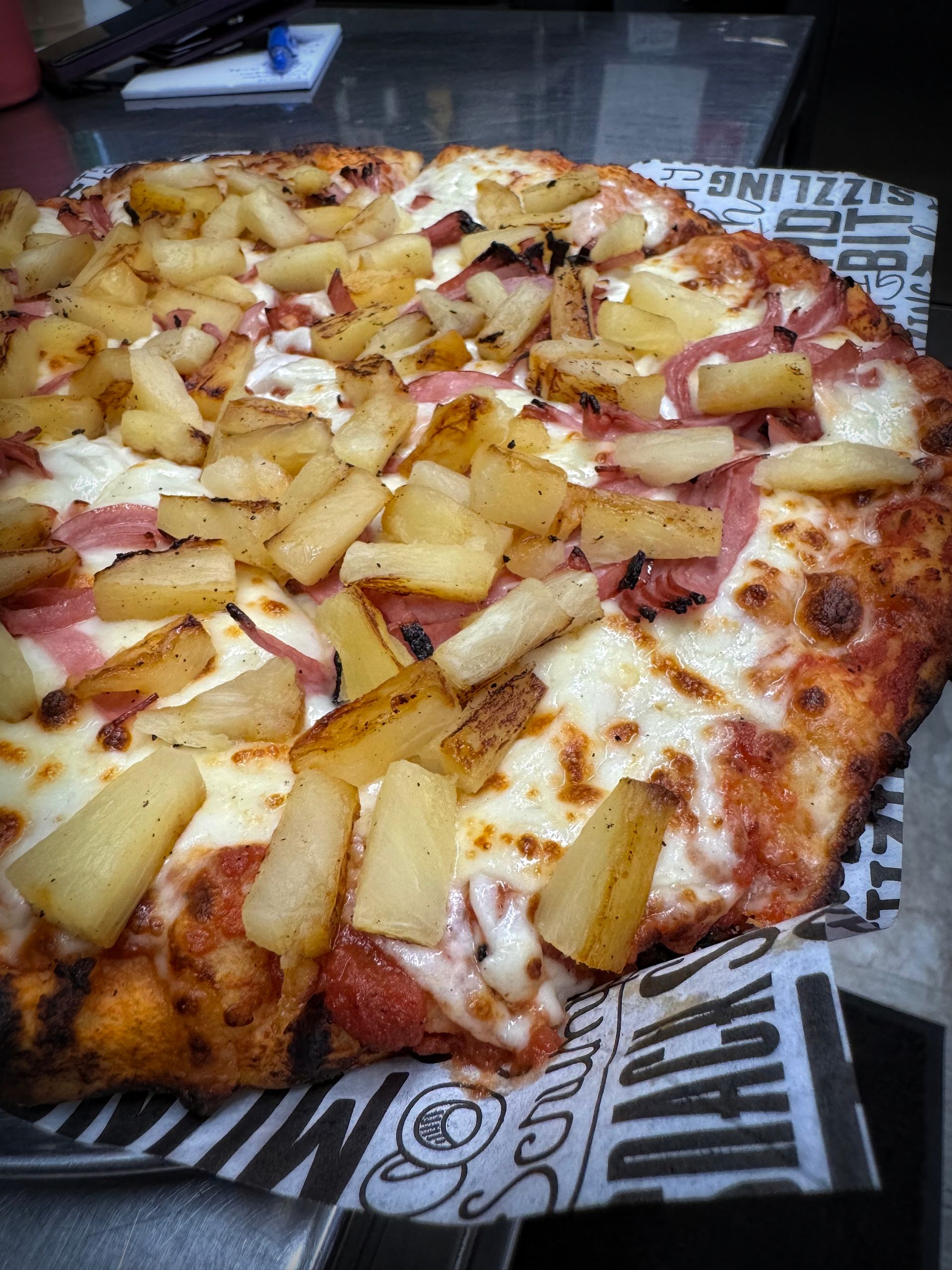 Pizza topped with pineapple and ham, on a patterned paper.
