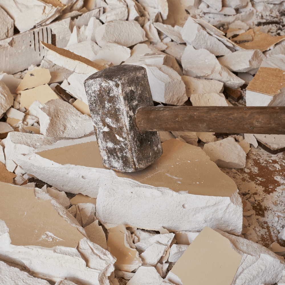 Sledgehammer on light-colored broken debris, likely drywall or plaster.