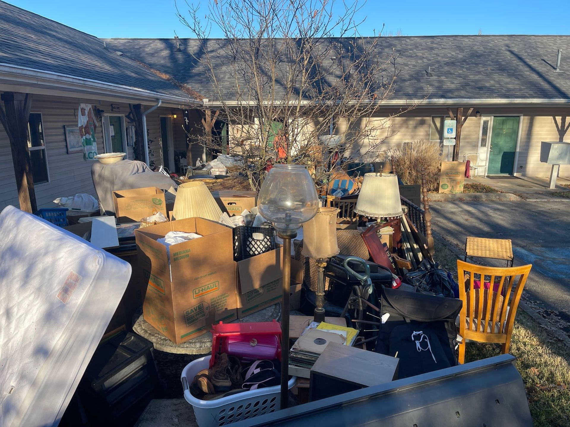 Pile of discarded items outside a building: boxes, furniture, lamps, and other debris.