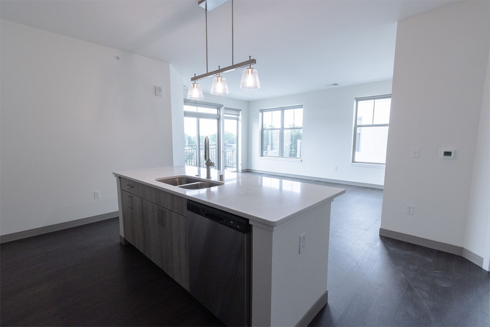 Modern kitchen with island, stainless steel appliances, and dark flooring. White walls and large windows.