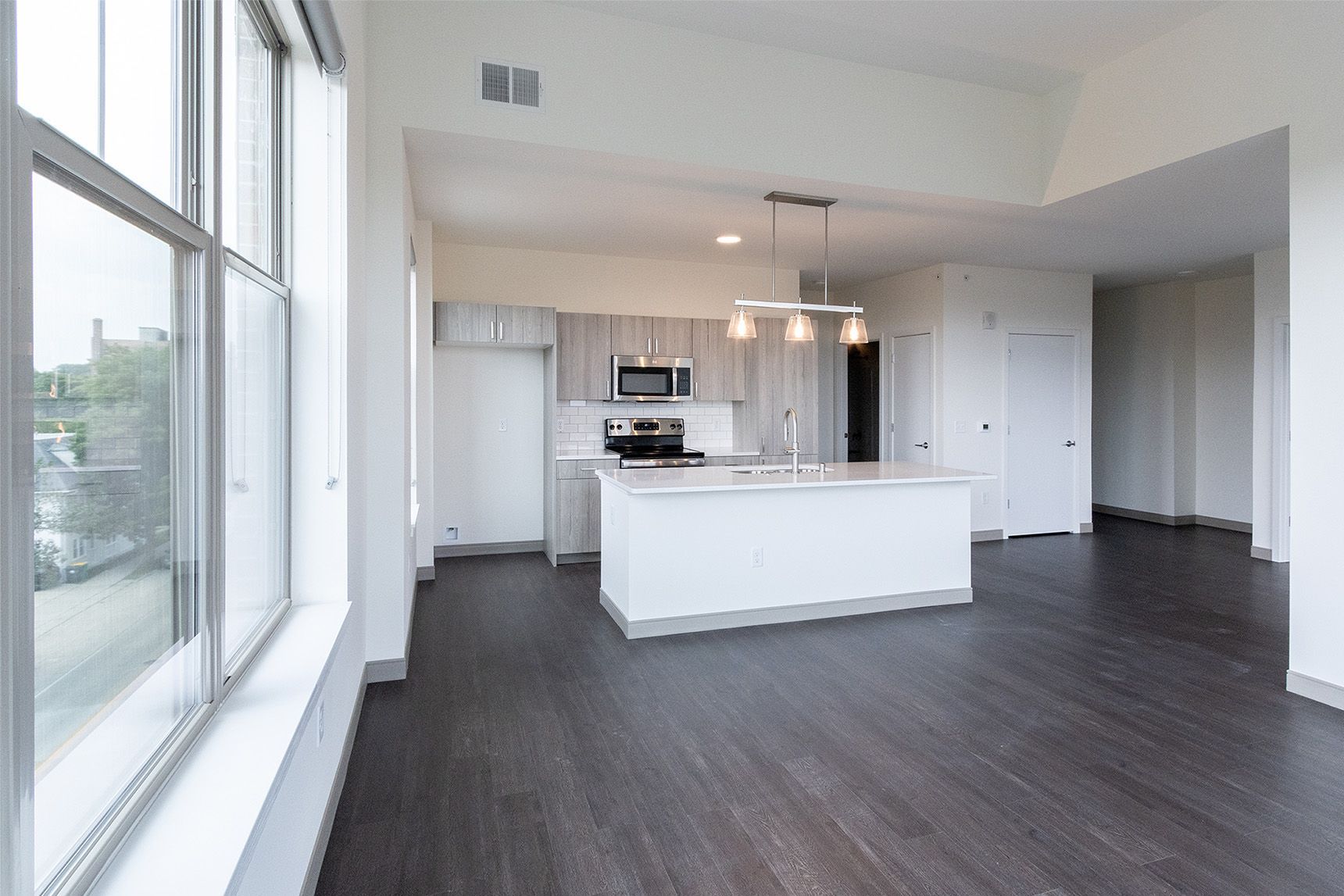 Modern open-plan kitchen and living area with gray cabinets, a white island, and dark hardwood floors.