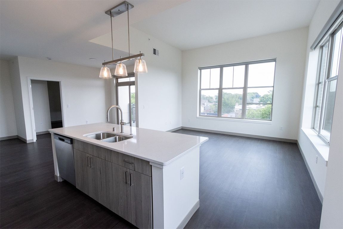 Modern kitchen with island, stainless steel appliances, and large windows.