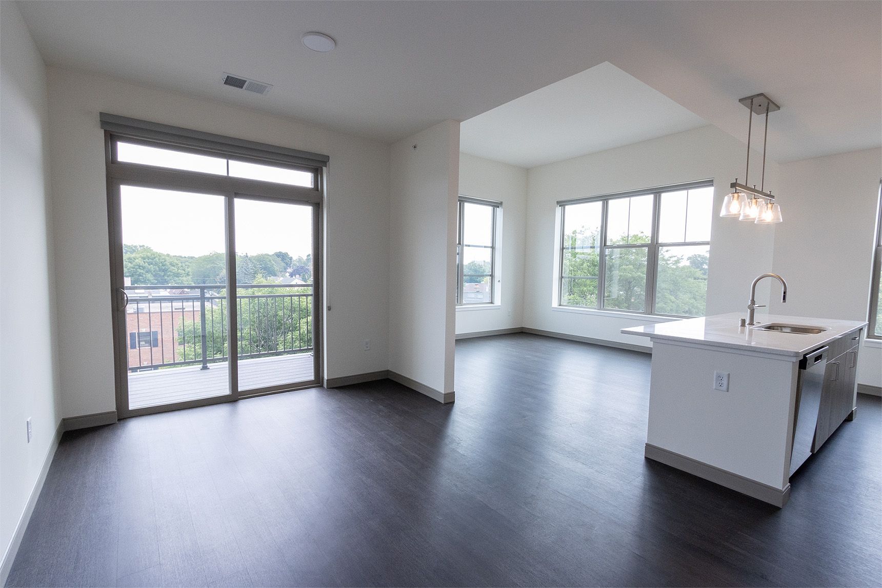 Modern apartment interior with dark floors, sliding glass door to balcony, and a white kitchen island.