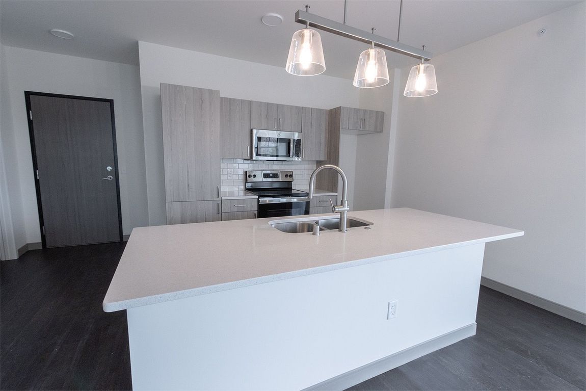 Modern kitchen with light cabinets, stainless steel appliances, white island, and pendant lights.