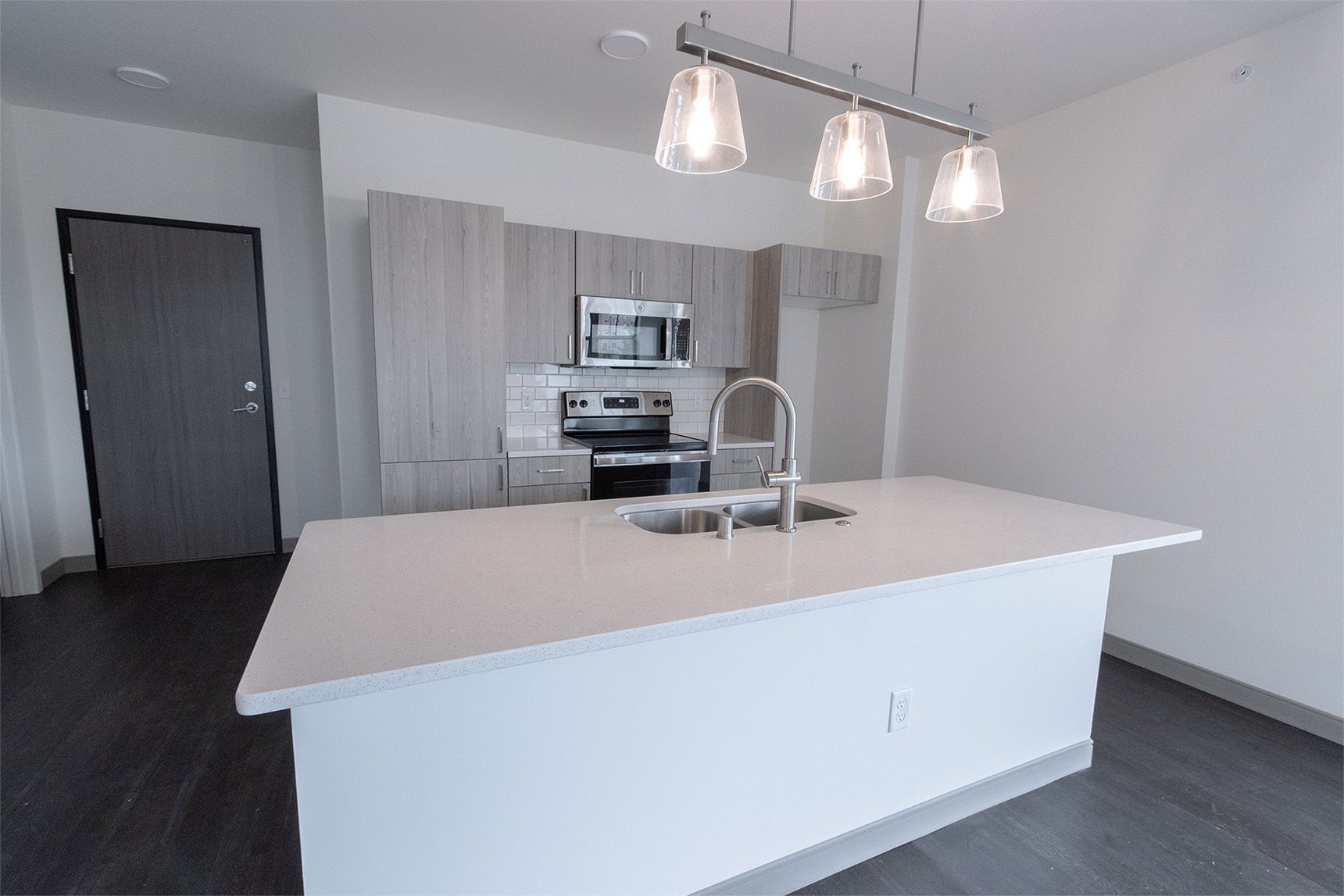 Modern kitchen with light cabinets, stainless steel appliances, white island, and pendant lights.