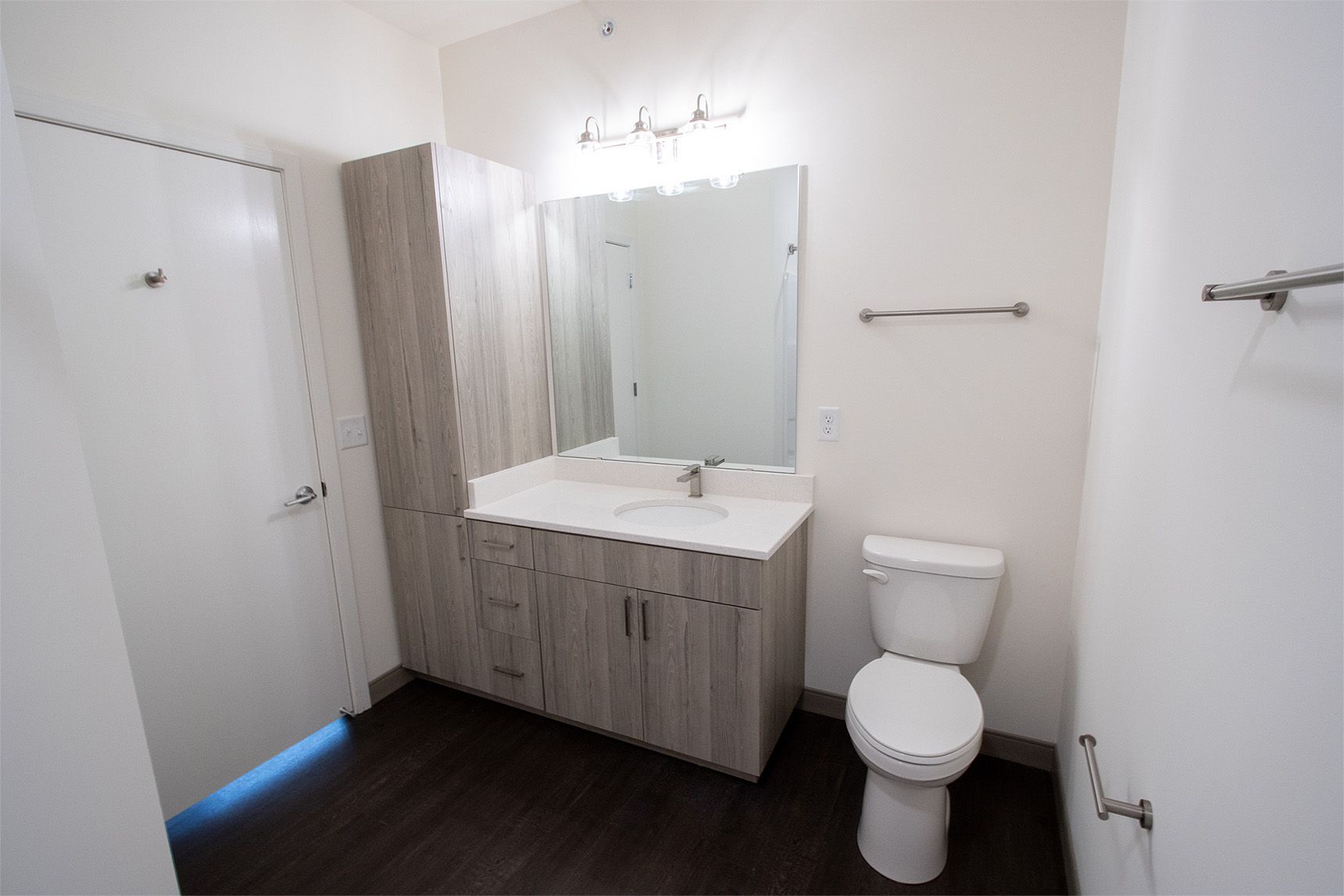 Bathroom with sink, toilet, and tall cabinet. White walls, wood-look floor, silver fixtures.