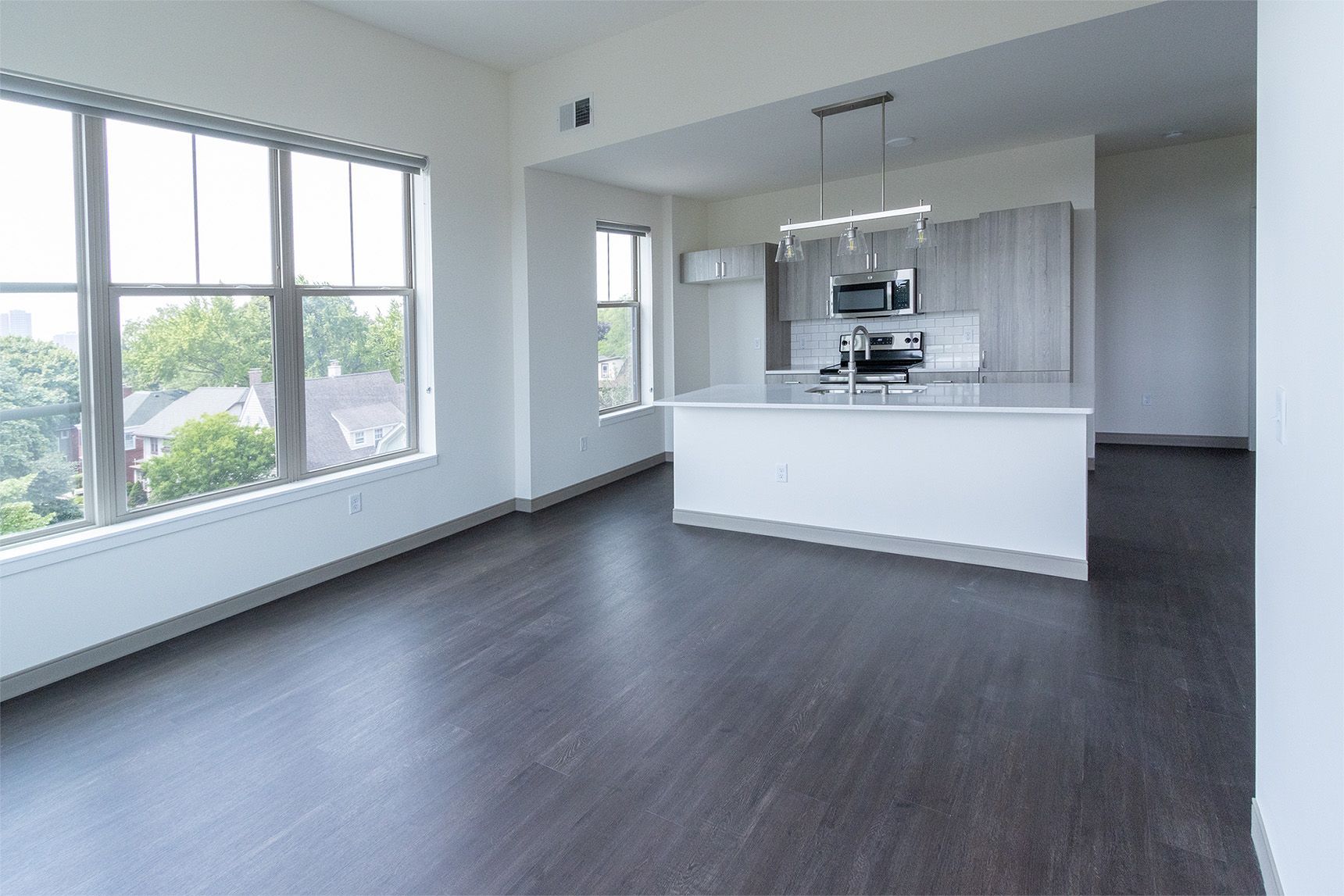 Empty modern apartment with dark wood floors, white walls, and kitchen island.