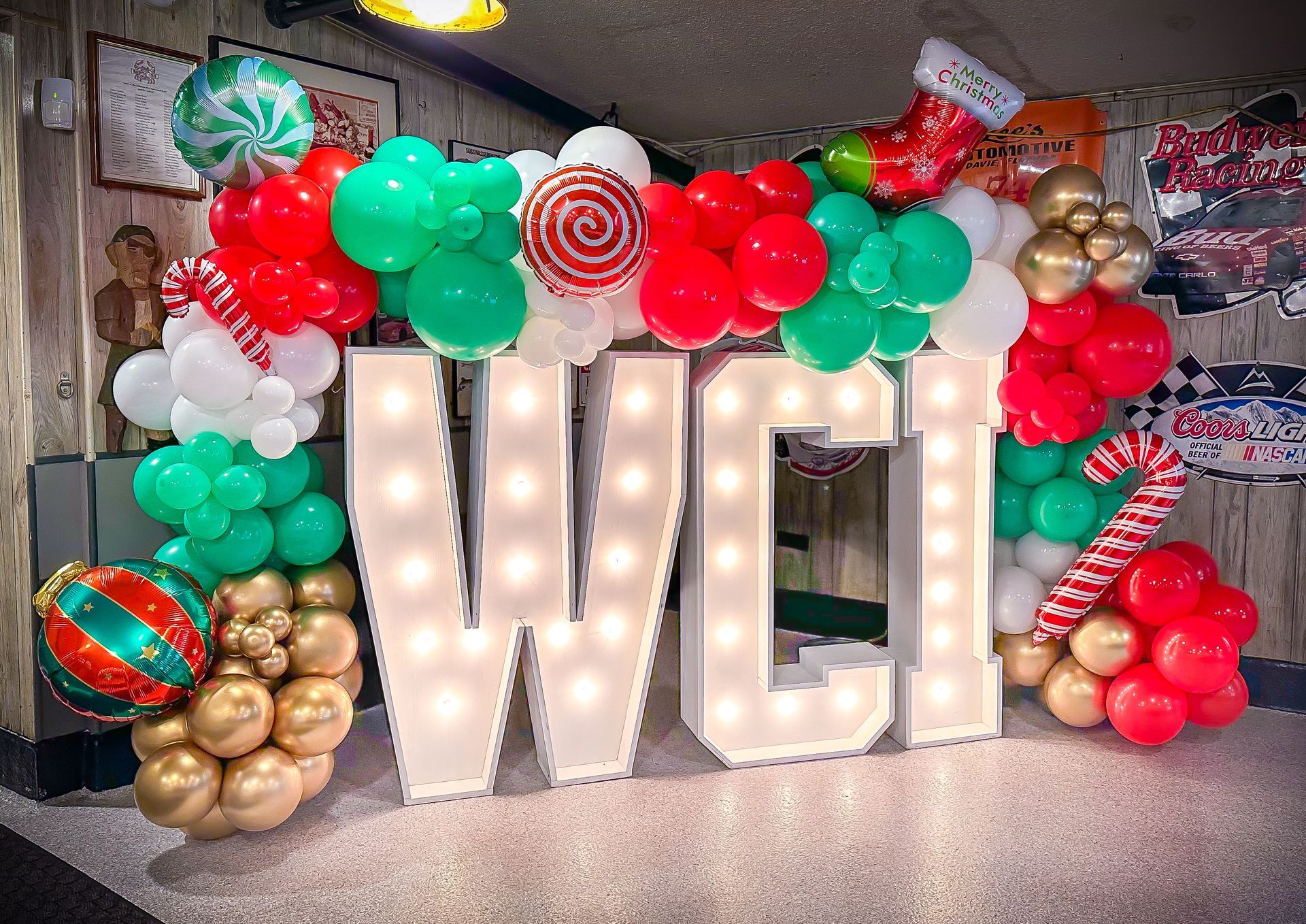 A large lighted letter w is surrounded by balloons and candy canes.