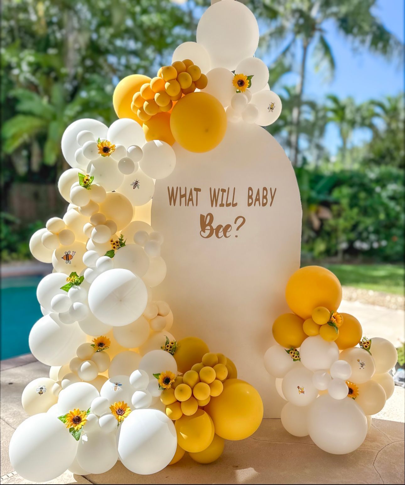 A sign that says `` what will baby bee '' is surrounded by yellow and white balloons.